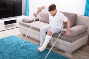 a young man in a leg cast getting off the couch